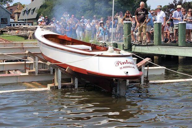 The draketail Pintail touches water for the first time at her launching at Chesapeake Bay Maritime Museum. The smoke is from a celebratory cannon fired in her honor.